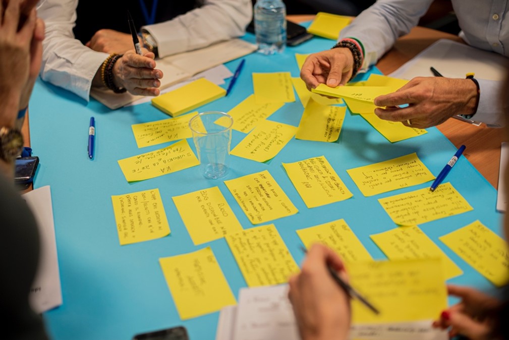 Four people writing on yellow post it notes and placing them on a blue paper.