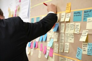 A person in black suit writing on a post it note on a board.