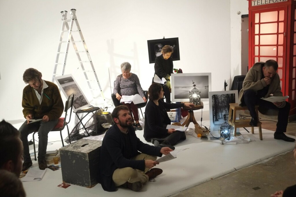 six people working on a theatre project in a white room with a red telephone box and other miscellaneous stuff.