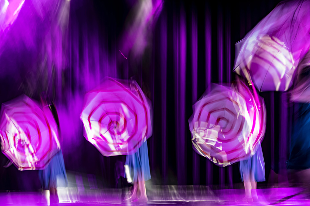 Dancers holding umbrellas and circling them on a stage, motion blur, pinkish background