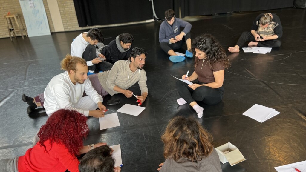 Emerging theatre artists working together, sitting on the floor and filling in documents.